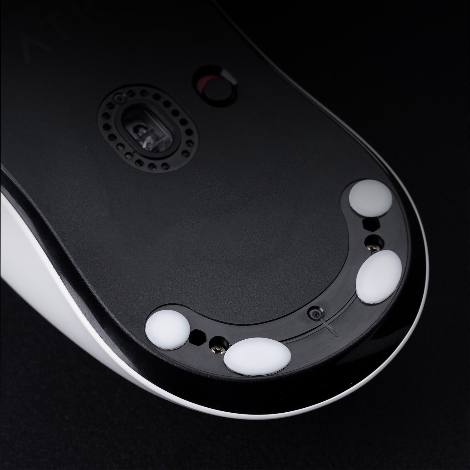 Bottom view of a white and black gaming mouse, showing PTFE feet and optical sensor.