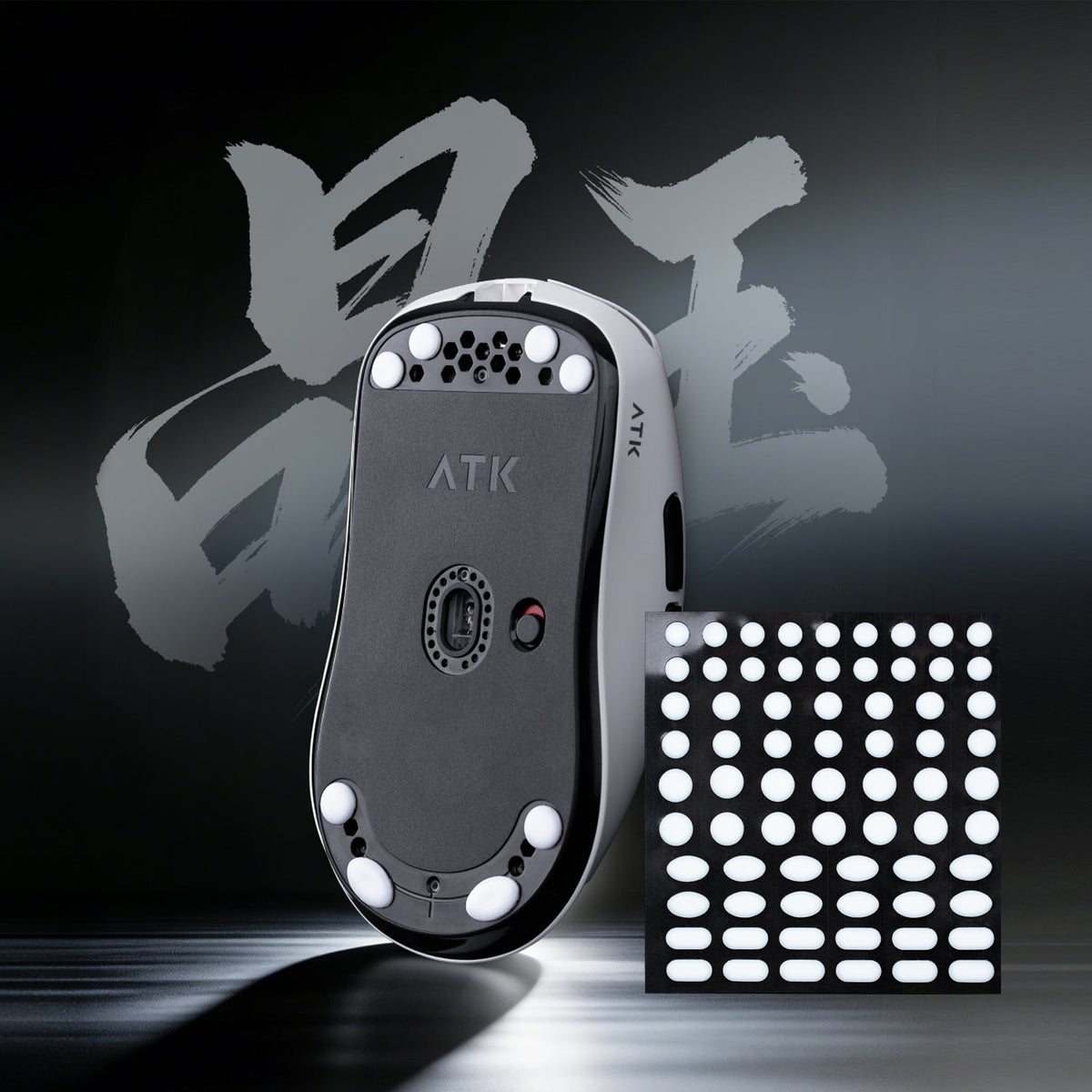 Bottom view of an ATK gaming mouse with white glide feet and a sheet of replacement glide stickers.