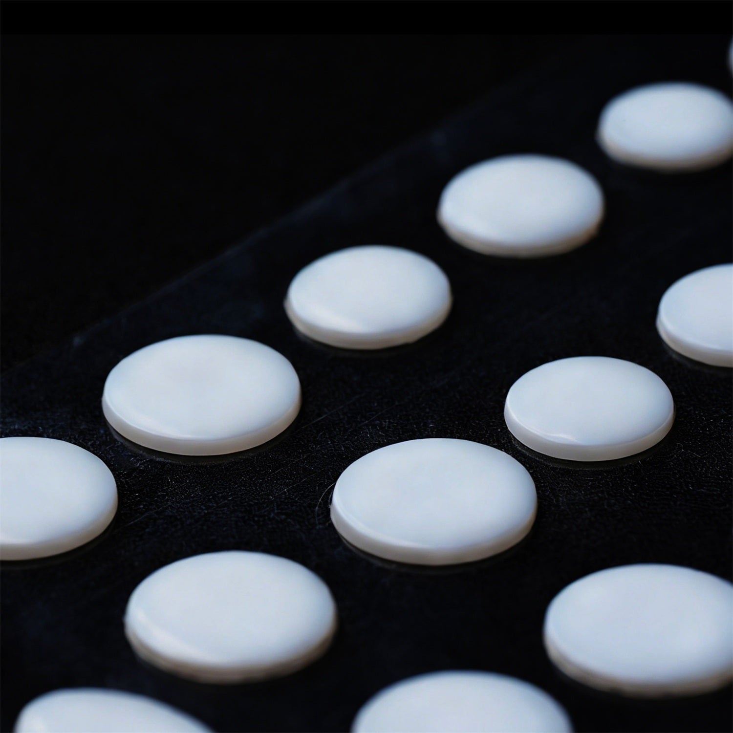 A close-up shot of multiple round, white, flat-topped objects arranged on a dark, textured surface.